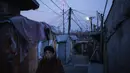 Seorang wanita berjalan melalui gang di desa kumuh Guryong, di distrik mewah Gangnam, Seoul, 24 Januari 2016. Di Guryong, mayoritas bangunannya adalah bangunan semi permanen yang dibangun dari bahan-bahan bekas konstruksi. (AFP PHOTO/Ed Jones)