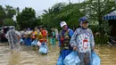 Orang-orang membawa makanan sambil berdiri di jalanan yang terendam banjir setelah hujan deras di Hoi An, Vietnam, Kamis 30 Oktober 2025. Pihak berwenang setempat terus melakukan upaya evakuasi ribuan penduduk dan wisatawan karena meluapnya Sungai Hoai, yang melintasi Hoi An. (NHAC NGUYEN/AFP)