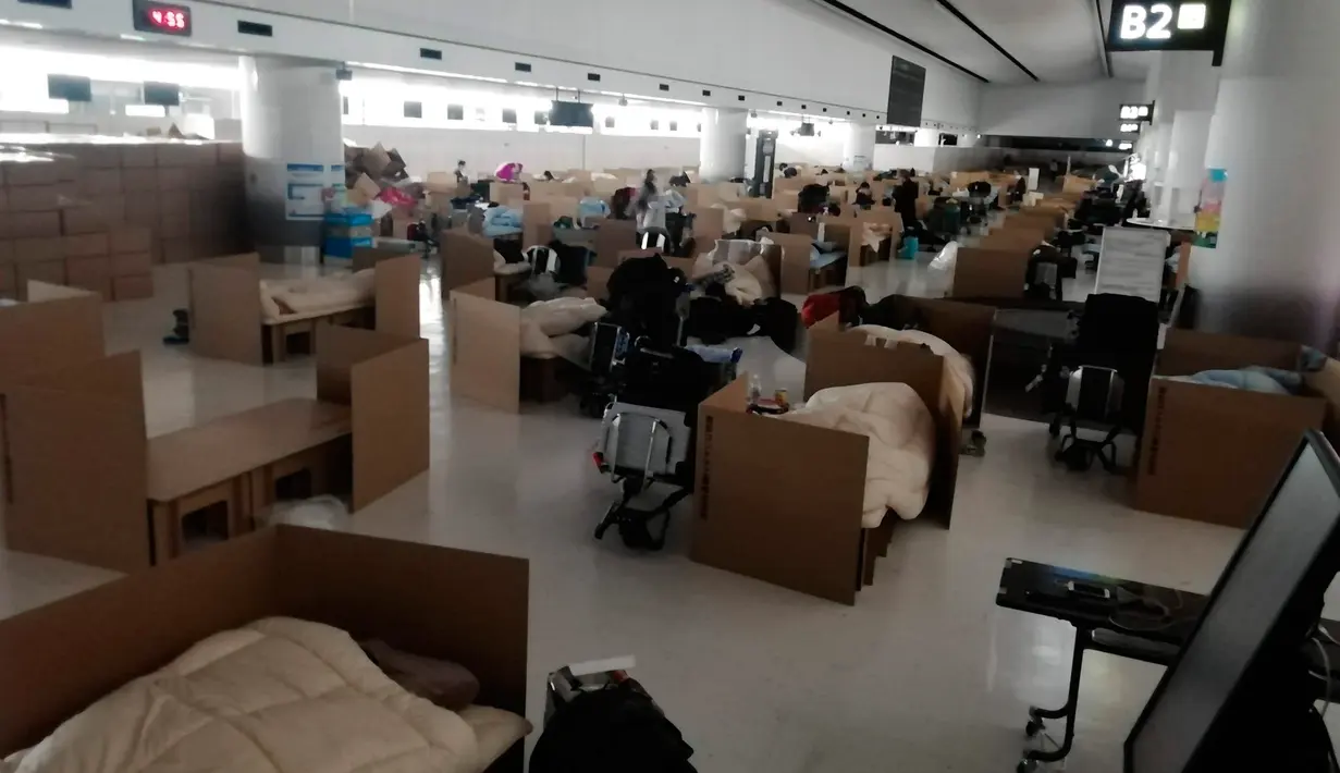 Orang-orang menunggu hasil tes virus corona mereka di tempat tidur sementara dari kotak kardus di Bandara Internasional Narita di Narita, dekat Tokyo, 8 April 2020. Bandara tersebut kini dipenuhi dengan bilik-bilik kardus yang berada di area pengambilan bagasi. (Naohiro Katsuta via AP)