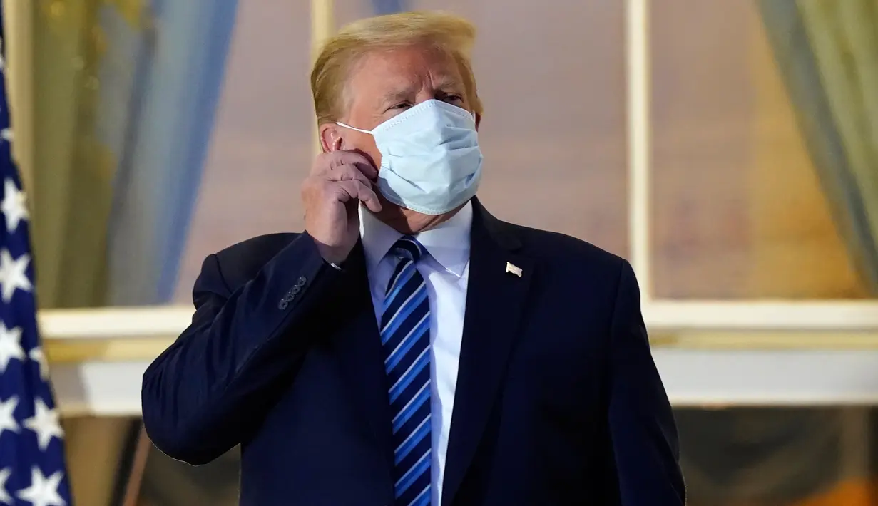 Presiden AS Donald Trump melepas maskernya saat berdiri di balkon di luar Blue Room setelah kembali ke Gedung Putih, Washington, Senin (5/10/2020). Donald Trump meninggalkan Walter Reed National Military Medical Center, rumah sakit tempat dia menjalani perawatan COVID-19. (AP Photo/Alex Brandon)