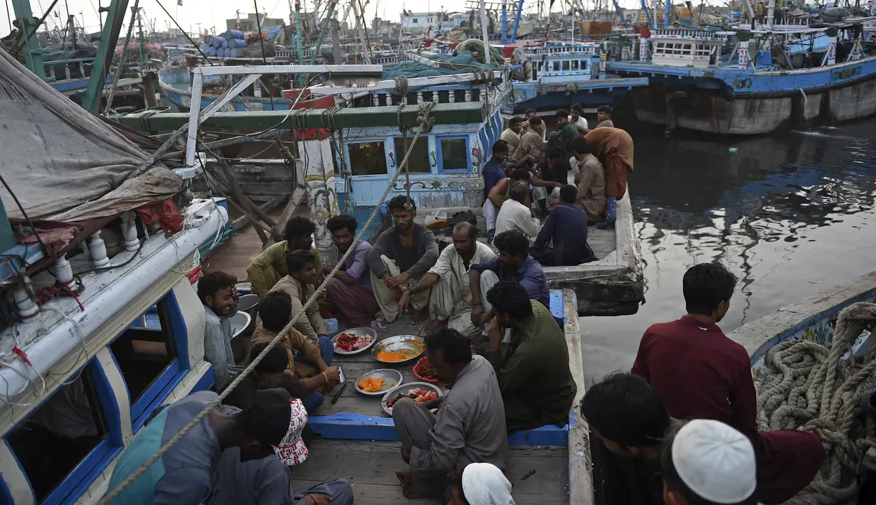 Nelayan duduk di atas kapal saat mereka berdoa sebelum berbuka puasa selama bulan suci Ramadhan di galangan kapal di kota pelabuhan Karachi, Pakistan pada 18 April 2022. Setelah menjalani ibadah puasa, waktu buka puasa menjadi momen yang dinanti oleh umat Islam. (Rizwan TABASSUM / AFP)