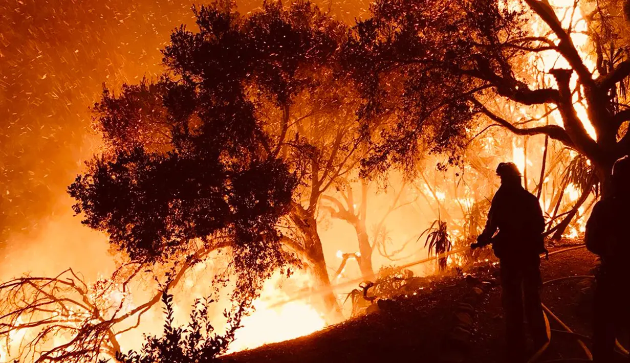 Petugas pemadam menyemprotkan air saat kebakaran melanda  rumah di atas Shepherd Mesa Road di Carpinteria, California (10/12). kebakaran ini telah melahap lahan dan rumah selama berhari-hari. (Mike Eliason/Santa Barbara County Fire Department via AP)