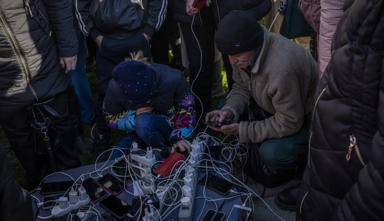 Warga berkumpul di sebelah hotspot internet di Kherson, Ukraina selatan, Senin (14/11/2022). Pada Jumat (11/11) lalu, Rusia telah menarik kembali lebih dari 30 ribu tentaranya di wilayah selatan. (AP Photo/Bernat Armangue)