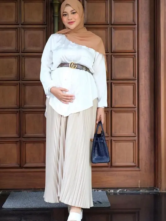 Agar terlihat lebih stylish, kamu bisa tambahkan aksesori berupa ikat pinggang saat memadukan kemeja dengan rok pleats seperti Aurel Hermansyah kala hamil ini. (Instagram/aurelie.hermansyah).