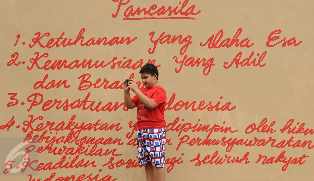 Seorang anak mengabadikan tulisan Pancasila di Lapangan Kebagusan, Jakarta, Rabu (15/2). Jelang menggunakan hak pilihnya pada Pilkada, Ketua Umum PDI-P Megawati Soekarnoputri menggoreskan tinta pada salah satu gambar. (Liputan6.com/Helmi Fithriansyah)