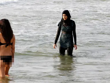 Seorang wanita mengenakan burkini di Laut Mediterania, Tel Aviv, Israel (30/8). Para wanita hijab ini tetap santai di tengah keramaian wanita berbikini. (REUTERS / Baz Ratner)