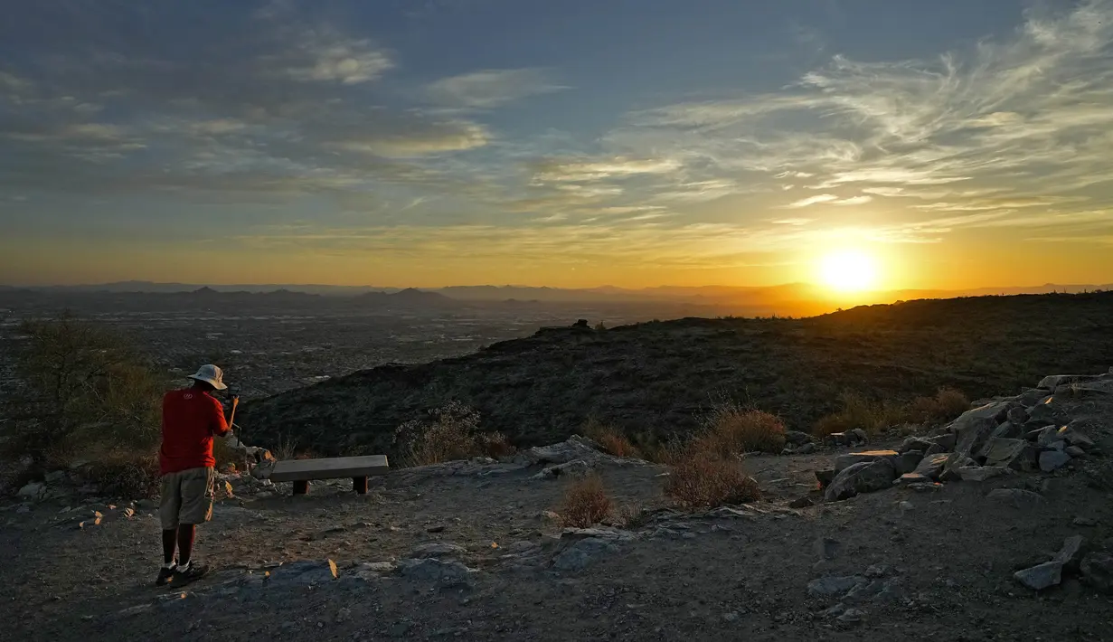 Seorang pejalan kaki memotret matahari terbit di atas Lembah di puncak South Mountain, Phoenix, Senin (17/7/2023). (AP Photo/Matt York)