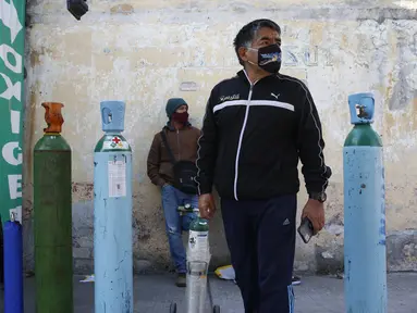 Jorge Perez antre mengisi tangki oksigen untuk anggota keluarga yang sakit COVID-19 di Mexico City pada 27 Desember 2020. Lonjakan pasien yang dirawat karena infeksi virus corona di Mexico City membuat toko pasokan medis kekurangan pasokan isi ulang tabung oksigen. (AP Photo/Ginnette Riquelme)
