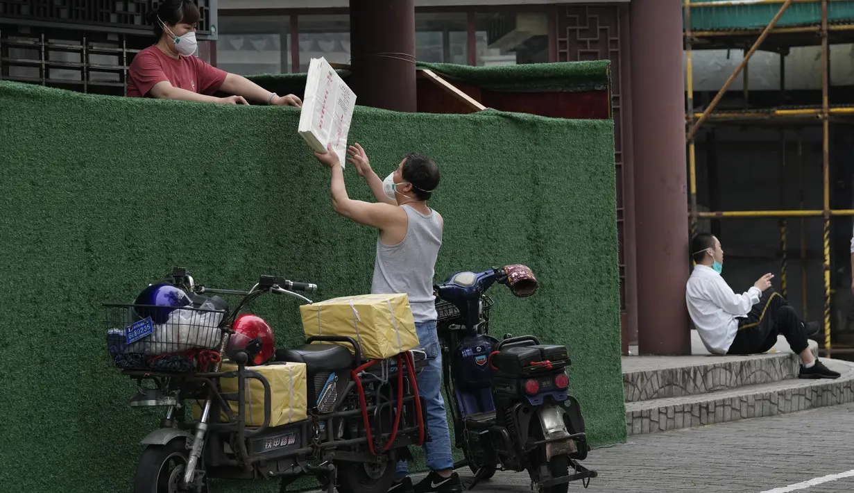 Seorang pria memberikan materi kepada seorang wanita melintasi penghalang yang dibangun di sekitar sebuah komunitas di Shanghai (2/6/2022). Lalu lintas, pejalan kaki dan pelari muncul kembali di jalan-jalan Shanghai ketika kota terbesar di China mulai kembali normal di tengah pelonggaran penguncian COVID-19 dua bulan. (AP Photo/Ng Han Guan)