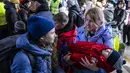 Seorang perempuan menggendong anak yang tidur saat menunggu transportasi lebih lanjut di stasiun kereta api di Przemysl, Polandia, 17 Maret 2022. Lebih dari tiga juta warga Ukraina telah melarikan diri melintasi perbatasan, kebanyakan perempuan dan anak-anak, menurut PBB. (Wojtek RADWANSKI/AFP)