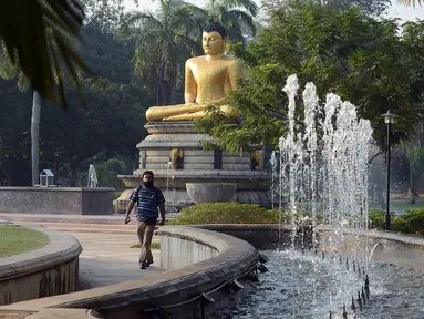 Seorang pria berjalan di depan patung Buddha di Taman Viharamahadevi di Kolombo, Sri Lanka (3/1). Taman tertua dan terbesar dari Pelabuhan Kolombo, terletak di depan gedung Balai Kota bergaya kolonial. (AFP Photo/Lakruwan Wanniarachchi)