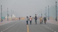 Pejalan kaki berjalan di sepanjang jalan dekat Gerbang India atau India Gate di tengah kabut asap tebal di New Delhi, Kamis (3/11/2022). Kabut asap di New Delhi mencapai tingkat hazardous (berbahaya) pada Kamis 3 November 2022. (Photo by Money SHARMA / AFP)