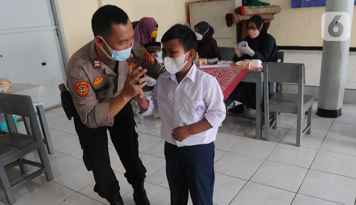 Anggota Polsek Cinere mendampingi murid kelas II saat vaksinasi covid-19 di SDI Al Hidayah, Depok, Selasa (25/1/2022). Mengantisipasi meningkatnya kasus Omicron, pemerintah mempercepat vaksin untuk lansia dan anak-anak, baik itu vaksin dosis pertama, kedua, maupun booster. (merdeka.com/Arie Basuki)