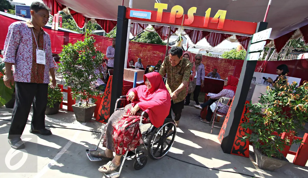 Petugas mendorong kursi roda seorang warga saat menggunakan hak pilih pada pemungutan suara Pilkada Depok di TPS Kampung Pilkada RW 03, Depok, Jawa Barat, Rabu (9/12). (Liputan6.com/Immanuel Antonius)