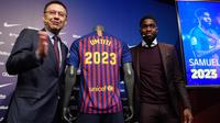 Bek Prancis, Samuel Umtiti dan Presiden Barcelona Josep Maria  berpose di samping jersey Barcelona pada pengumuman perpanjangan kontraknya di stadion Camp Nou, Senin (4/6). Umtiti memperpanjang kontraknya bersama Barcelona hingga 2022. (LLUIS GENE/AFP)