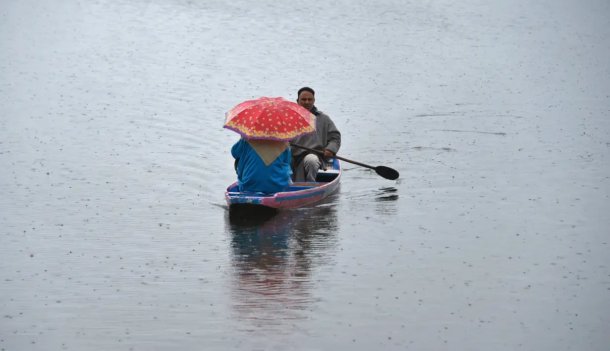 Seorang awak perahu Kashmir mengangkut penumpang saat hujan di Danau Dal di Srinagar (20/3). Di Sepanjang tepi Danau Dal terdapat Ghate yang merupakan tempat bersandarnya Shikara. (AFP Photo/Tauseef Mustafa)