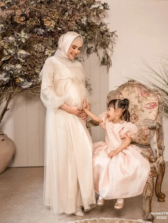 Dalam sesi pemotretan ini, Kartika Putri tanpil anggun mengenakan gaun panjang warna pinggala tanpa motif yang dilapisi kain transaparan dengan ujung lengan mengembang. Penampilannya disempurnakan dengan jilbab polos berwarna senada. “Mother and daughter gemes session,” tulis Rio Motret bersama foto ini, pada Selasa (9/8/2022). (Foto: Dok. Instagram @riomotret)