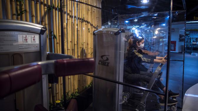 Orang-orang berolahraga dengan plastik penyekat untuk membatasi jarak antar pengunjung di sebuah tempat gym di Surabaya, Rabu (21/10/2020). Pusat kebugaran itu dibuka dengan menerapkan protokol kesehatan sebagai pencegahan COVID-19. (Juni Kriswanto / AFP)