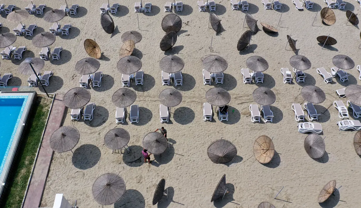 Foto udara pada 1 Juni 2020 menunjukkan para pekerja memasang payung jerami di sebuah pantai di Qerret, dekat kota Kavaja, Albania. Rencananya pada 6 Juni mendatang, semua pantai umum akan dibuka untuk wisatawan setelah Albania menerapkan langkah-langkah pelonggaran pencegahan virus corona. (SHKULLA