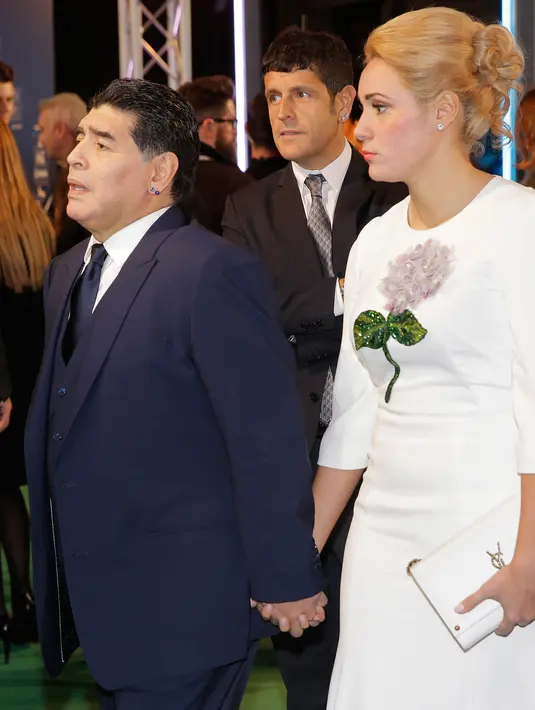 Pesepakbola legendaris Argentina, Diego Maradona mengandeng tangan kekasihnya, Rocio Oliva saat tiba menghadiri The Best FIFA Football Awards 2017 di London, (23/10). Rocio Oliva merupakan mantan pemain sepak bola wanita. (AP Photo/Alastair Grant)