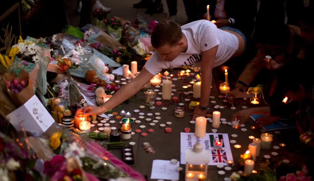 Seorang pria menyalakan lilin sehari setelah serangan bunuh diri di sebuah konser Ariana Grande di Albert Square, Manchester, Inggris, (23/5). Kejadian ini menyebabkan 22 orang tewas  dan melukai 119 lainnya. (AP Photo/Emilio Morenatti)