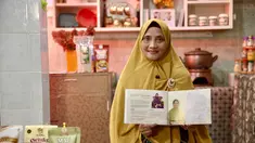 Dewi Aminah, pendiri Iswara Food, berdiri di depan rak produknya yang rapi tersusun di ruang produksi rumahnya di Solo. Usaha ini ia rintis setelah kehilangan bisnis batik akibat kebakaran di Pasar Klewer. (Adv/BRI)