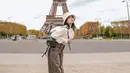OOTD gemas dari Fuji dengan latar Menara Eiffel. Ia mengenakan tank top putih ditumpuknya dengan cropped sweater, dan wide-leg jeans abu-abu. Penampilannya semakin manis dengan padu padan sneakers dan bucket hat. [Foto: Instagram/fuji_an]