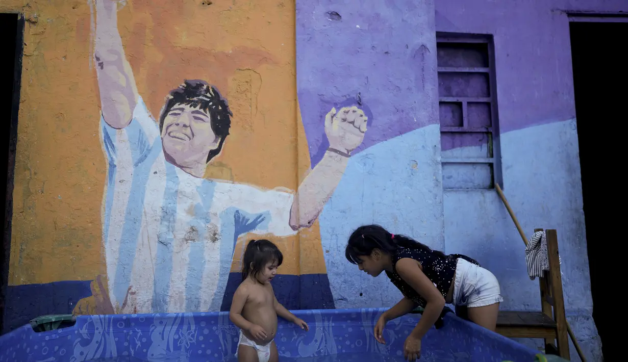 Seorang gadis menyegarkan diri di kolam anak-anak di luar rumahnya dengan mural mendiang pemain sepak bola Diego Maradona di Buenos Aires, Argentina, Kamis, 2 Maret 2023. (AP Photo/Natacha Pisarenko)