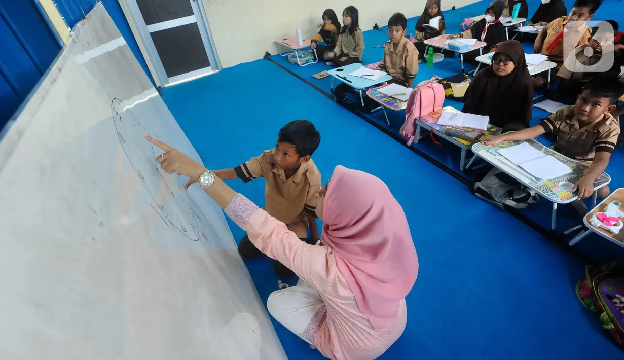 Seorang guru mengajar murid tanpa menggunakan meja dan kursi sekolah, di SDN Bojong Nangka 02, Kabupaten Bogor, Jawa Barat, Kamis (16/2/2023). Sudah lebih dari dua pekan, murid-murid di tiga ruang kelas  menerapkan kegiatan belajar mengajar beralas karpet karena belum tersedianya bangku dan meja. (merdeka.com/Arie Basuki)