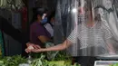 Penjual sayuran menerima pembayaran dari balik tirai plastik untuk mencegah virus corona di sebuah pasar di kota Quezon, Filipina, Selasa (22/9/2020). Presiden Rodrigo Duterte mengatakan telah memperpanjang status masa darurat Covid-19 di negaranya hingga satu tahun ke depan. (AP Photo/Aaron Favila)