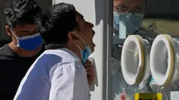 Seorang pria membuka maskernya untuk melakukan swab tenggorokan COVID-19 secara rutin di tempat pengujian virus corona di Beijing, Selasa (6/9/2022). Saat ini ada 33 kota di China yang berada dalam situasi lockdown sebagian atau penuh karena wabah COVID-19. (AP Photo/Andy Wong)