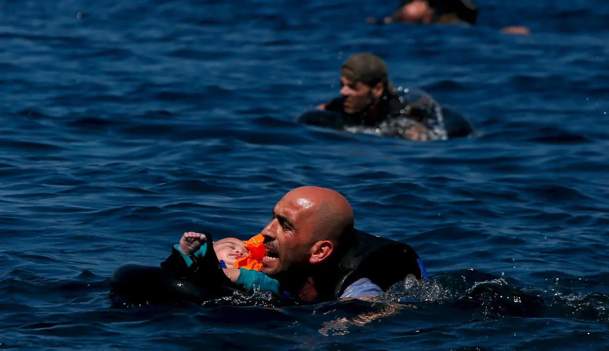 Seorang pengungsi Suriah menggendong bayi sambil berenang menuju pantai setelah perahu yang mereka naiki kempes sebelum mencapai pulau Yunani Lesbos, 12 September 2015. (REUTERS/Alkis Konstantinidis)  