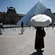 Seseorang berlindung di bawah payung di depan museum Louvre di Paris saat gelombang panas yang memecahkan rekor melanda sebagian besar Eropa Barat pada Kamis 28 Mei 2026. (SIMON WOHLFAHRT/AFP)