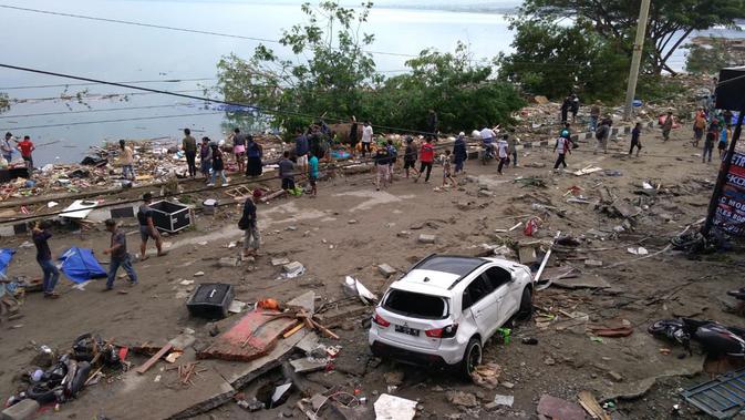 Orang-orang berjalan melewati mayat (penutup biru) setelah gempa dan tsunami di Palu, Sulawesi Tengah , Sabtu (29/9). Gelombang tsunami setinggi 1,5 meter yang menerjang Palu terjadi setelah gempa bumi mengguncang Palu dan Donggala. (AFP /OLA GONDRONK)