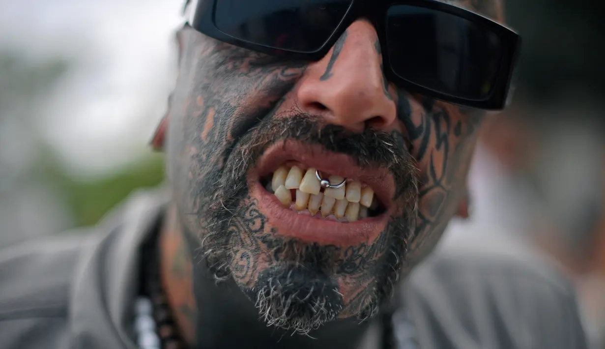 Seorang pria menunjukka anting yang ada di dekat giginya serta wajah yang dipenuhi tato saat acara Tattoo Week tahunan di Rio de Janeiro, Brasil (12/1). (AFP Photo/Mauro Pimentel)