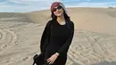 Mengunjungi gurun pasir, Azizah tampil mengenakan dress hitam panjang dipadukan outer panjangnya. [@azizahsalsha_]