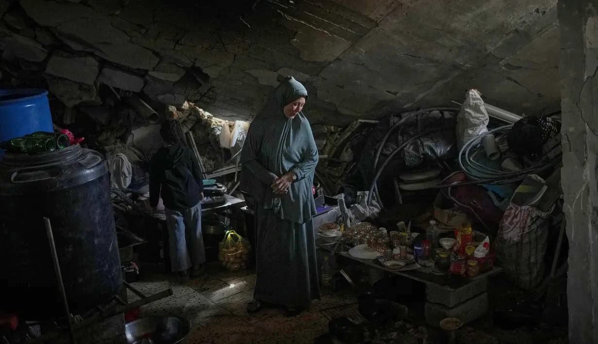 Hingga Desember 2025, sekitar 92% unit hunian dan 352.000 rumah di Gaza telah hancur atau mengalami kerusakan parah. Tampak dalam foto, Khadija Abu Shaqfa dan putrinya Rita berjalan melewati dapur rumah mereka yang rusak, di mana makanan dan peralatan makan berserakan di antara reruntuhan, di Jabaliya, Kota Gaza, Jumat, 21 November 2025. (AP Photo/Jehad Alshrafi)