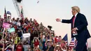 Presiden Donald Trump melemparkan masker dari atas panggung ke kerumunan pendukung saat berkampanye di Bandara Internasional Orlando Sanford di Sanford, Florida, Senin (12/10/2020). Donald Trump kembali berkampanye untuk pertama kalinya usai dinyatakan negatif Covid-19. (AP Photo/Evan Vucci)