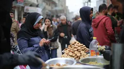 Terlihat upaya warga tetap berupaya menjaga semangat hari kemenangan dengan berbelanja kebutuhan pokok dan persiapan Idul Fitri 1447 Hijriah. Tampak dalam foto, seorang perempuan pengungsi Palestina menggunakan telepon seluler sambil berbelanja di pasar jalanan sekitar kamp pengungsi Nuseirat, Jalur Gaza tengah, pada Rabu 18 Maret 2026. (Eyad Baba/AFP)