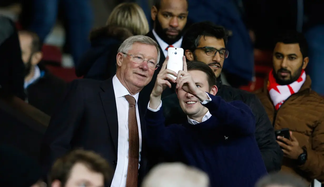 Mantan manajer Manchester United Sir Alex Ferguson berselfie dengan fans saat menyaksikan pertandingan antara Manchester United dengan Chelsea di Stadion Old Trafford, Inggris (28/12). MU bermain imbang dengan Chelsea dengan skor 0-0. (Reuters/Phil Noble)