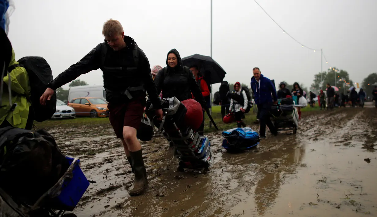 Penonton Festival Glastonbury tampak melewati jalanan yang banjir dan berlumpur saat tiba di Worthy Farm, Somerset, Inggris , (22/6).Meski cuaca hujan, Para penonton tetap akan menyaksikan festival musik paling populer di dunia. (REUTERS / Stoyan  Nenov)