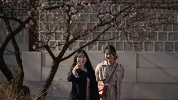 Dua wanita menggunakan ponsel berselfie di istana Changdeokgung di Seoul , Korea Selatan (2/4). Korea Selatan sedang bersiap untuk meluncurkan jaringan seluler 5G pertama di dunia pada 5 April. (AFP Photo/Ed Jones)