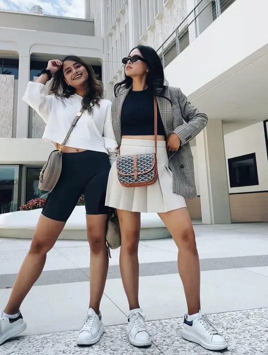 Berpose dengan sang adik, Maudy Ayunda kasual semi formal dengan outfit bernuansa abu-abu putih. Mengenakan croptop hitam dan blazer kotak-kotak, Maudy nampak feminin dengan rok rampel berwarna putih. Ia pun mengalungkan tas Goyard Belvedere PM dengan harga sekitar Rp20-30jutaan. (Instagram/maudyayu