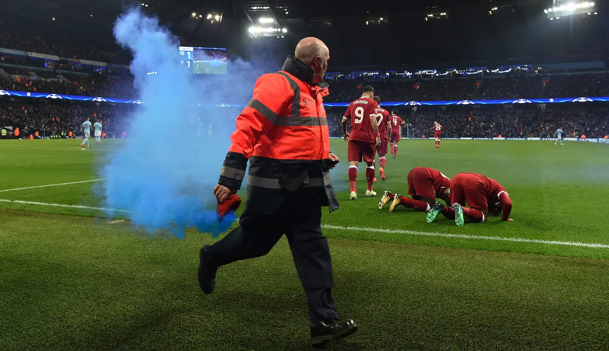 Seorang petugas mengambil flare saat pemain Liverpool Mohamed Salah bersama rekannya Sadio Mane melakukan selebrasi usai mencetak gol ke gawang Manchester City dalam pertandingan Liga Champions di Etihad Stadium (10/4). (AFP/Paul Ellis)