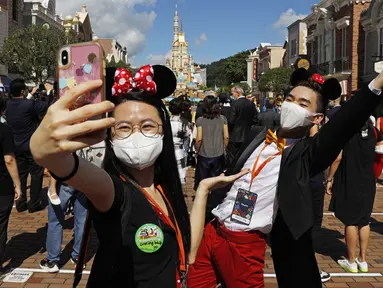Para pengunjung yang mengenakan masker untuk mencegah penyebaran COVID-19 berswafoto di Disneyland Hong Kong, Kamis (18/6/2020). Disneyland Hong Kong kembali beroperasi pada 18 Juni 2020 dengan menerapkan sejumlah protokol kesehatan baru. (AP Photo/Kin Cheung)