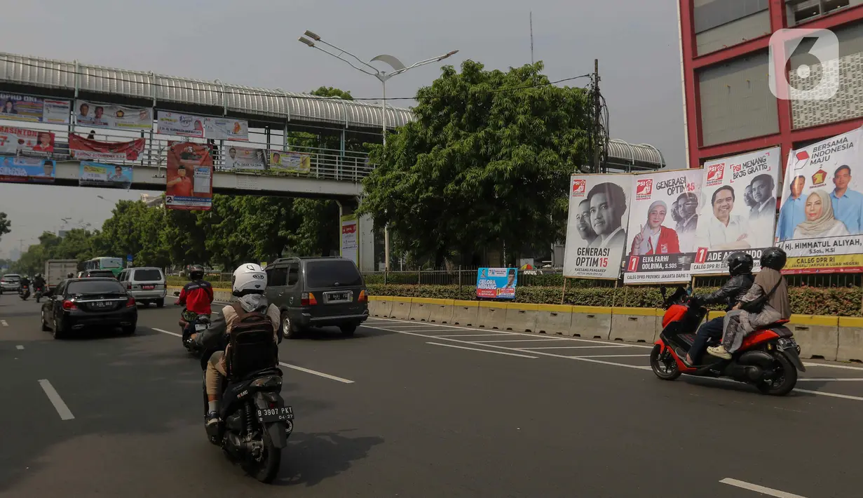 Pengendara kendaraan bermotor melintas dekat Alat Peraga Kampanye (APK) yang terpasang di kawasan Salemba, Jakarta, Kamis (7/12/2023).  (Liputan6.com/Herman Zakharia)