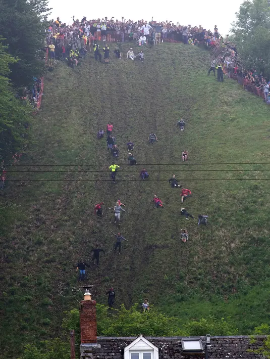 Peserta berlari menuruni bukit curam untuk mengejar keju dalam kompetisi Cheese Rolling di Cooper's Hill di Brockworth, Gloucestershire, Inggris, Senin (28/5). Peserta berebut 1,5 kilogram keju yang digelindingkan dari atas bukit. (Aaron Chown/PA via AP)