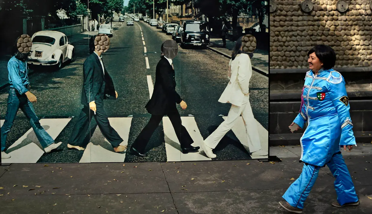 Seorang wanita melewati sebuah gambar nyata saat kegiatan untuk memecahkan rekor dunia dengan jumlah terbesar orang mengenakan pakaian dan bergaya seperti  The Beatles di sebuah taman di Mexico City, Meksiko 28 November 2015. (AFP PHOTO/ALFREDO ESTRELLA)