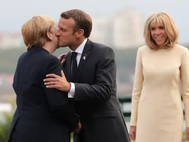 Presiden Prancis Emmanuel Macron (tengah) mencium Kanselir Jerman Angela Merkel (kiri) disaksikan istrinya Brigitte Macron (kanan) yang di KTT G7, Biarritz, Prancis, Sabtu (24/8/2019). KTT G7 beragenda pertahanan demokrasi, kesetaraan jender, pendidikan, dan lingkungan. (AP Photo/Markus Schreiber)