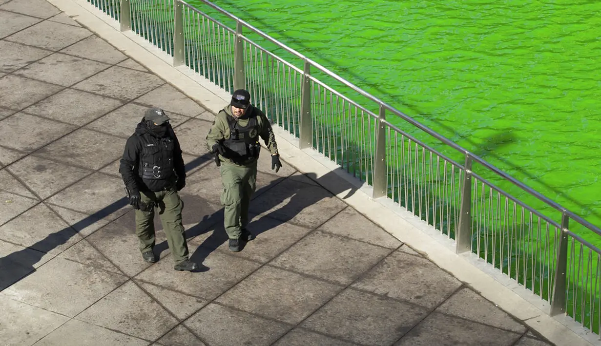 Petugas keamanan berjalan di sepanjang Riverwalk yang ditutup untuk umum setelah Sungai Chicago diwarnai hijau jelang Hari Santo Patrick di Chicago, Amerika Serikat, Sabtu (13/3/2021). Setiap tahunnya, pewarnaan Sungai Chicago selalu menarik wisatawan. (Pat Nabong/Chicago Sun-Times via AP)